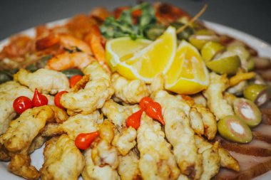 Renkli deniz ürünleri tabağında kızarmış balık, karides, zeytin ve kırmızı biberle süslenmiş limon dilimleri var. Mutfak keşfi ve yemek deneyimleri için mükemmel.