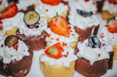 Krem şantili renkli mini tatlılar ve çilek ve yaban mersini de dahil olmak üzere taze meyveler beyaz bir tabakta, şenlikli toplantılar için ideal.