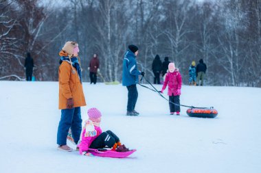 Valmiera, Letonya - 11 Ocak 2026: Aile üyeleri kış etkinliklerine katılıyor, çocuklar kızakla kayıyor ve karlı arazide oynuyorlar, neşeli anılar yaratıyorlar