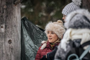 Ligatne, Letonya - 11 Ocak 2026: Kürk şapkalı ve kırmızı ceketli genç sarışın kadın karda arkadaşlarıyla neşeli bir anı paylaşıyor