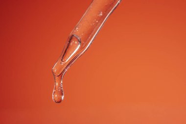 Sıvı içeren temiz damlatıcı parlak turuncu arkaplanın üzerine asılmış, bilimsel araçların güzelliğini ve deneysel hassasiyet sanatını gözler önüne seriyor.