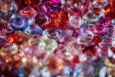 Çeşitli şekil ve renklerde çeşitli parlayan taşlar yansıtıcı bir yüzey üzerinde yakın bir şekilde düzenlenmiştir. Kırmızı, mavi, pembe ve berrak renkli canlı renkler sergilerler.