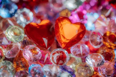 İki kırmızı kalp şeklindeki değerli taş renkli kristallerin ve mücevherlerin arasına yerleşerek dekoratif kullanım için çarpıcı ve canlı bir bileşim oluşturur.