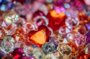 Parlak değerli taşlar ve kristallerden oluşan canlı bir koleksiyonda merkezde çeşitli renkli taşlarla çevrili kırmızı kalp şeklinde önemli bir mücevher bulunur.