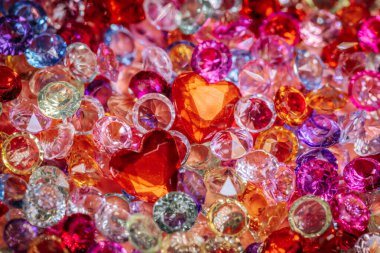 Kırmızı kalpler de dahil olmak üzere çeşitli renk ve şekillerde çeşitli parlak taşlar ve kristaller dekoratif amaçlar için yansıtıcı bir yüzeye saçıldı.