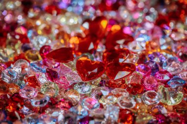 Kırmızı kalp şeklindeki kristallerle çeşitli pırıl pırıl parlayan değerli taşlar parlak bir zemin üzerinde parlak ve renkli mücevherler arasında fotokopi uzayı ile görsel olarak çekici bir görüntü yaratıyor.