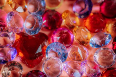 Kırmızı kalp şeklinde bir mücevher içeren çeşitli pırlanta ve kristaller, yumuşak pembe bir arka planda sergileniyor, dekoratif veya tasarım kullanımı için ideal.