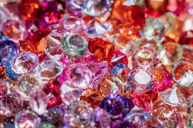 Kırmızı, pembe, mor ve berrak olmak üzere çeşitli şekil ve renklerde parlayan pırlanta taşlar, canlı bir şekilde birbirine yakın bir şekilde dizilmiş.