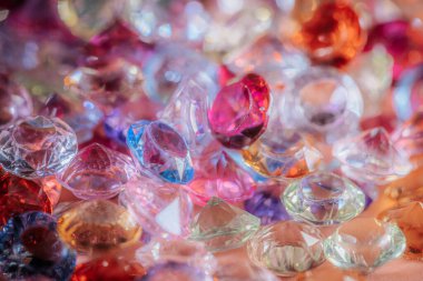 Çeşitli renklerde ve şekillerde çeşitli parlayan değerli taşlar bir yüzeye dağılmış, parlak ve yansıtıcı özelliklerini renkli bir görüntüyle vurguluyorlar.