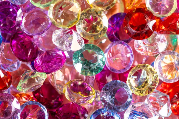 Çeşitli şekil ve renklerde çeşitli parlayan taşlar yansıtıcı bir yüzeye yakın bir şekilde yerleştirilmiş, parlak renkler ve karmaşık kesikler sergiliyor.