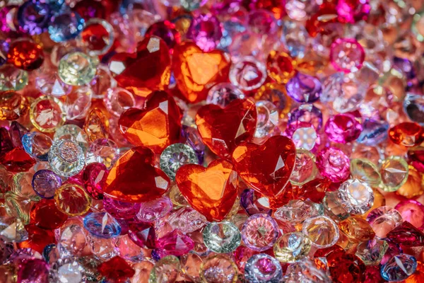 Kırmızı kalp şeklindeki taşlar da dahil olmak üzere çeşitli renk ve şekillerde çeşitli parlak taşlar ve kristaller dekorasyon için renkli bir yüzey üzerinde bir araya getirildi.