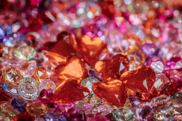 Kırmızı kalp şeklindeki kristallerin dekoratif düzende çeşitli canlı dekoratif taşlarla harmanlandığı renkli, pırıl pırıl değerli taşların görüntüsü.