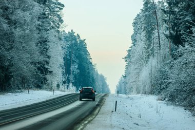 Valmiera, Latvia - January 21, 2026: Vehicle traveling along a snowy road flanked by trees covered in frost, capturing a serene winter scene