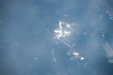 Mavi zemin üzerindeki ışığı yansıtan buz kristallerinin yakın görüntüsü, soğuk koşullarda oluşmuş eşsiz desenleri ve dokuları vurguluyor.