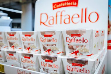 Raffaello şekerleme kutuları bir mağaza rafında düzgünce düzenlenmiş, kırmızı markalı beyaz ambalaj ve temiz bir perakende çevre sergileniyor
