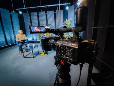 Valmiera, Letonya - 30 Ocak 2026: Sony video kamerası, dikey panelleri ve yeşillikleri görünen bir stüdyoda bir masada oturan sunucuya odaklanıyor