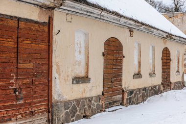 Terk edilmiş yapıda ahşap kapılar ve karla çevrili bir taş taban yer alıyor. Kırsal bir arazide yıpranmış dış ve eğimli çatıyı vurguluyorlar.