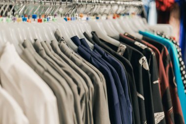 Perakende mağazasındaki askılarda çeşitli desenleri ve kumaş dokularını vurgulayarak birden fazla renk ve stilde düzenli gömlekler sergiliyorlar.