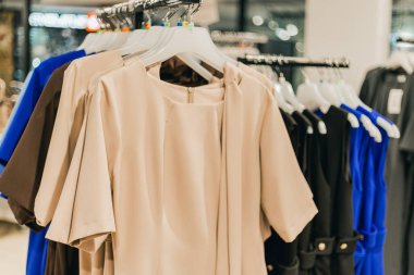 Modern bir perakende mağazasının içinde bej, siyah ve mavi elbiselerle şık kadın elbiseleri sergileniyor, moda kıyafetleri ve aksesuarları vurgulanıyor.