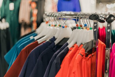 Perakende mağazasının içindeki bir askıda asılı çeşitli renklerde çeşitli giyim ürünleri, çeşitli stiller ve canlı renkler sergiliyor.