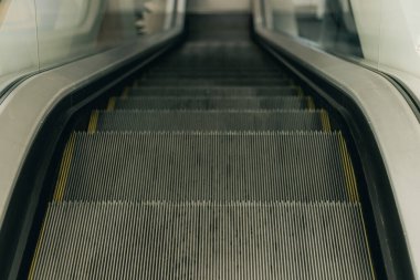 Çağdaş bir iç mekanda cam panellerle çevrili metal oyuklar ve sarı çizgiler içeren yürüyen merdivenlerin yakın çekimi.