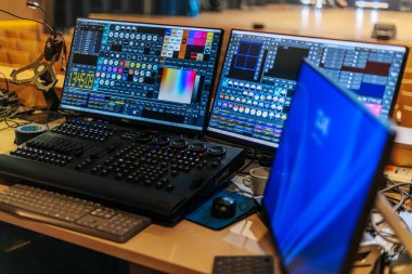 İki bilgisayar ekranı, çağdaş bir çalışma alanında elektronik cihazları ve araçları olan ahşap bir masanın üzerinde canlı yazılım arayüzleri ve kontrol panelleri gösterir