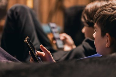 İki erkek çocuk koltukta otururken akıllı telefonlarıyla meşgul oluyorlar. Etrafı yumuşak ışıklı, sıcak tonlarla çevrili.