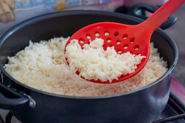 Mutfak düzeninde kırmızı kaşıkla tencerede beyaz pirinç pişirdim..