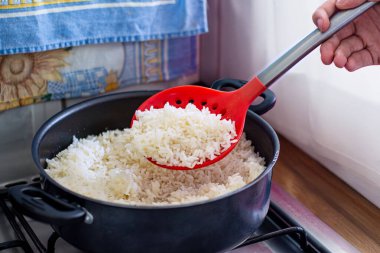 Mutfak düzeninde kırmızı kaşıkla tencerede beyaz pirinç pişirdim..