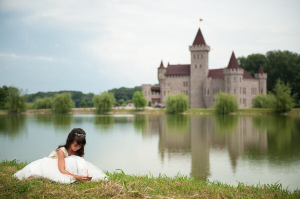 girl in a ball gown is sitting in front of the lake and the castle