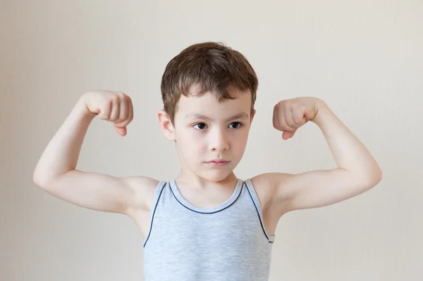 Серьезный маленький мальчик в футболке показывает мышцы — стоковое фото
