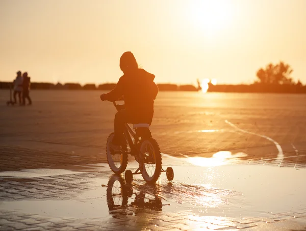 Kind rijdt fiets via de plas op de achtergrond van het instellen van de zon — Stockfoto