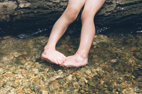 Kid holding feet in the river while sitting on log — Stock Photo, Image