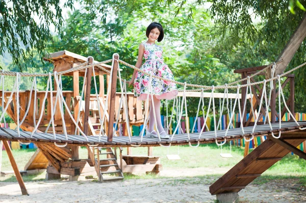 Linda menina de pé na ponte suspensa no parque infantil — Fotografia de Stock