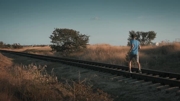 在跑步训练中 一名在球衣和短裤方面活跃的男子在农村地区沿着铁路跑步 以提高耐力 — 图库视频影像