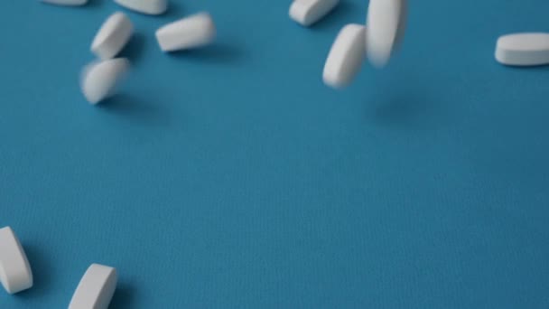 Veel witte tabletten pillen vallen neer op blauw oppervlak in slow motion — Stockvideo
