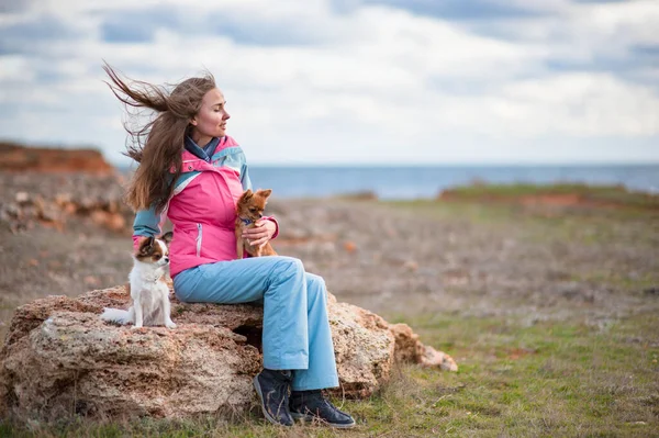 Dreamy girl sitting with two little dogs on cold sea shore with copy space — Stock Photo, Image