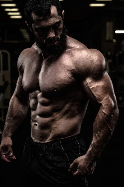 Strong sport athlete male with beard and perfect physique body in dark fitness gym — Stock Photo, Image