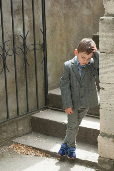 Copil trist pe fundalul unui perete vechi și scări cu o poartă — Fotografie, imagine de stoc