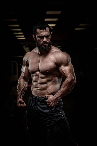Strong young bearded athlete male with perfect sport physique body torso muscle in dark fitness gym — Stock Photo, Image
