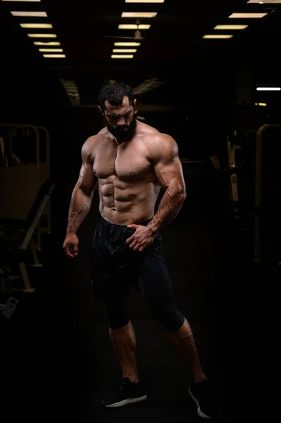 Sport lifestyle of strong young athlete bearded caucasian man with perfect athletic physique body torso abdominal and chest muscle in dark fitness gym — Stock Photo, Image