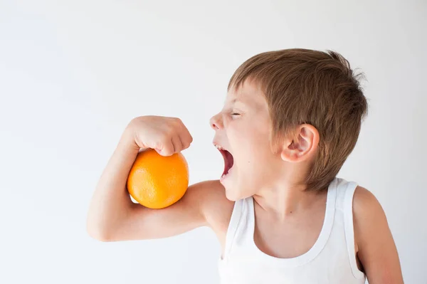 Băiețel cu fructe portocalii pe bicepși musculari care doresc să muște și să mănânce cu spațiu de copiere — Fotografie, imagine de stoc
