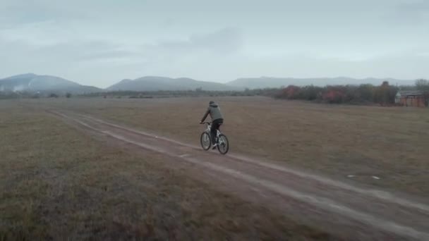 男子自行车道绿色夹克骑白色山地自行车沿着农村肮脏的道路灰尘从车轮通过田野木材秋天的夜晚 人类的踏板自行车在小径上前进 冒险生活方式的概念 — 图库视频影像