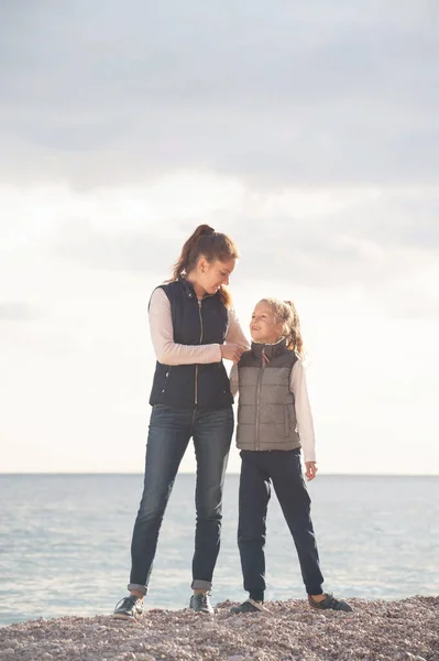 Felice famiglia caucasica di giovane madre donna che abbraccia la figlia indossando primavera autunno giacca collezione di moda sulla riva del mare al tramonto — Foto Stock