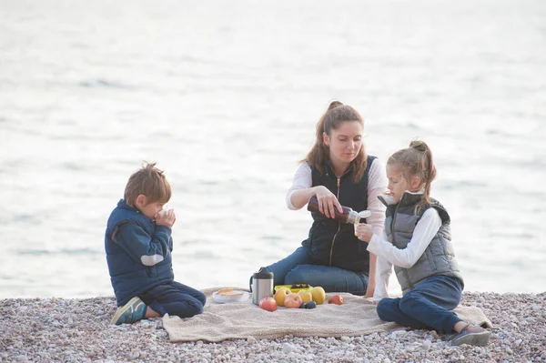 Famiglia caucasica attiva in giacca senza maniche seduta sulla spiaggia di mare a bere tè caldo durante i viaggi di vacanza all'aria aperta — Foto Stock