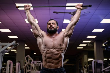 Spor salonunda barla esneme hareketleri yaparken güçlü genç bir erkek.