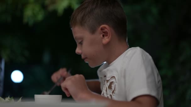 귀여운 소년 이 저녁에 야외 카페에서 수저와 디저트를 먹으며 맛있는 식욕 과 기쁨을 만끽 합니다. — 비디오