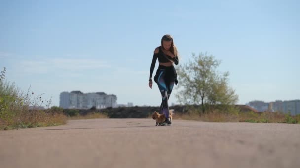Spor giyim sektöründe genç ve aktif bir kadın şehirde eğlence, gösteri, yürüyüş ve itaat trenleri sırasında küçük köpeğini bacaklarının altında çalıştırıyor. — Stok video