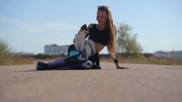 Pes a majitel sport žena přátelství sedí společně na asfaltové silnici ve městě se stromy během letní venkovní volnočasové aktivity relaxace — Stock video