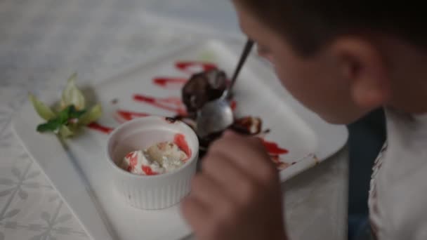 Маленький мальчик ест вкусную еду сладкий десерт с ложкой в ночном кафе — стоковое видео